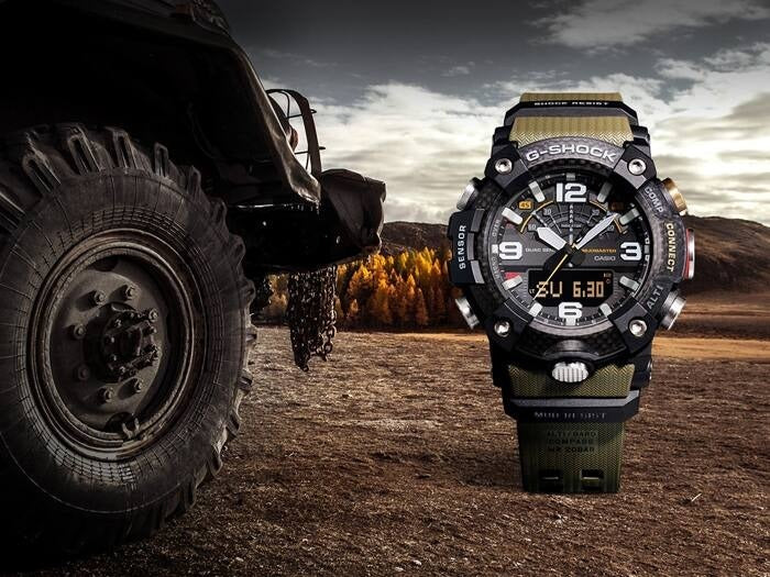 Casio G-Shock Mudmaster GG-B100-1A3DR watch beside an off-road truck tire, outdoor lifestyle shot