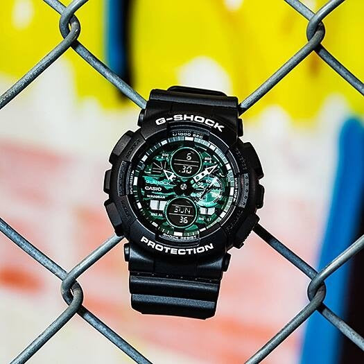 Casio G-Shock GA-140MG-1AER watch hanging on a chain-link fence, outdoor lifestyle shot