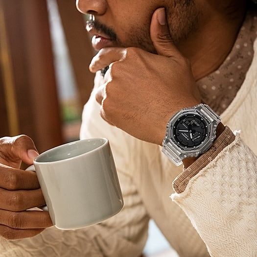 Casio G-Shock GA-2100SKE-7ADR transparent watch worn on wrist while holding a coffee mug, lifestyle shot
