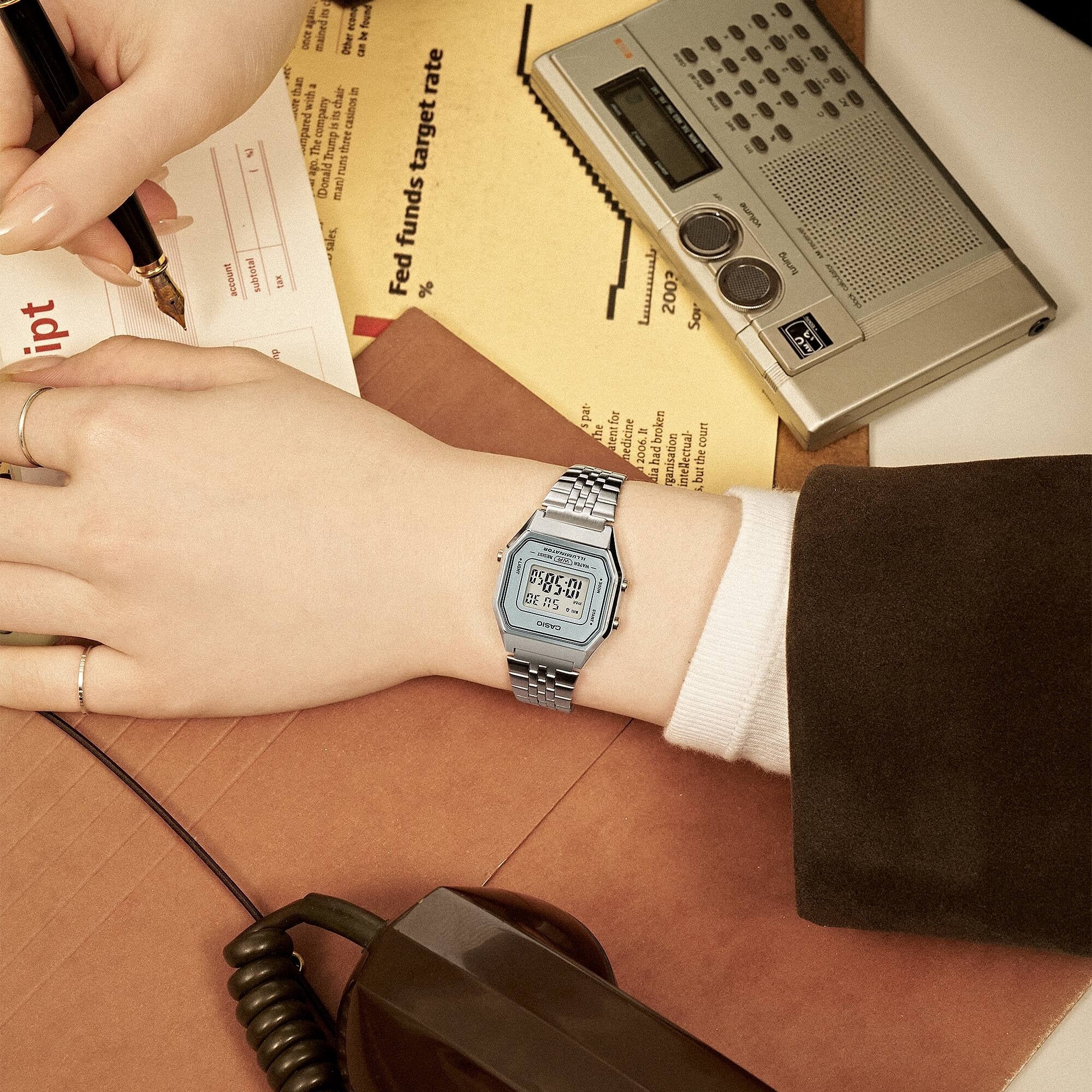 Casio Vintage LA680WA-7DF worn on wrist beside a vintage phone and radio, retro desk scene